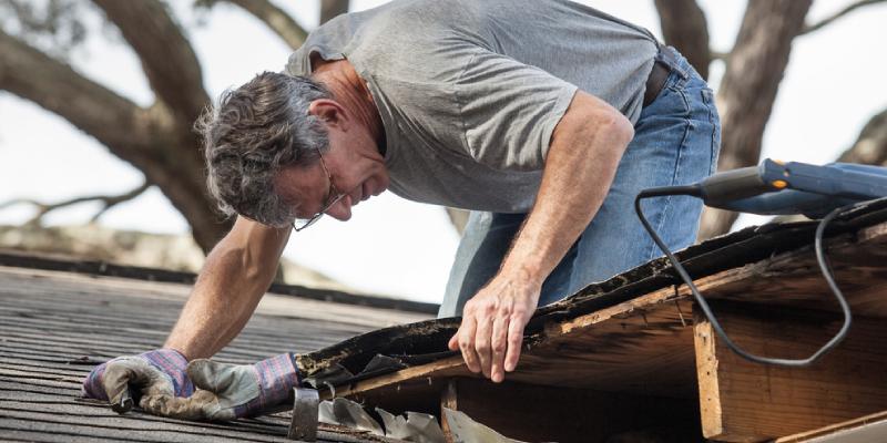 A photo of a man leaning over a roof, inspecting it for roof leaks