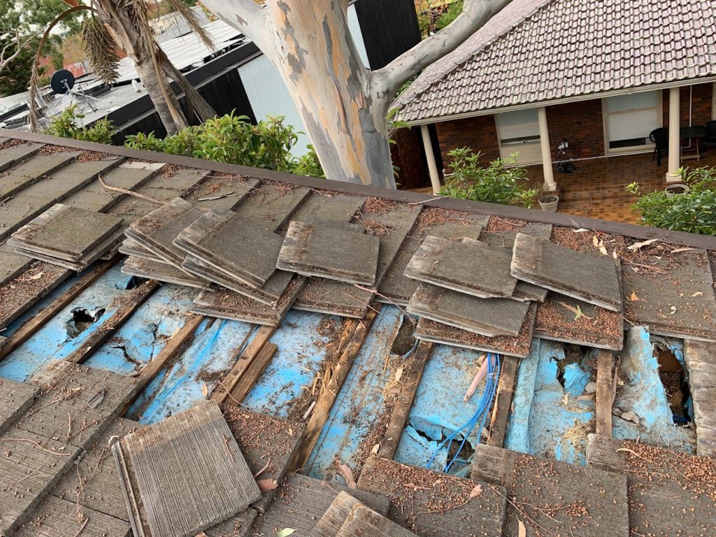 A photo of a roof with scattered wooden tiles and rotting timber battens beneath